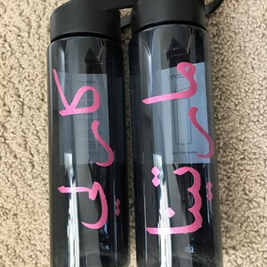 May include: Two black water bottles with pink lettering. The lettering on the left bottle says "J.J." and the lettering on the right bottle says "J.J. mac".