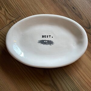May include: White oval ceramic dish with a black and white illustration of a bird's nest with eggs and the word "NEST." printed on it.