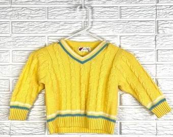 May include: Yellow cable knit sweater with blue and white trim. The sweater has a v-neck and long sleeves.