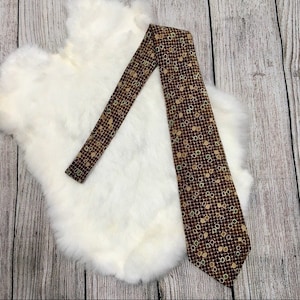 Pode incluir: Uma gravata de seda marrom com um padrão geométrico de círculos bege e verdes. A gravata está sobre um fundo de pele branca.