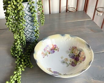 May include: A white porcelain bowl with a yellow rim and floral pattern. The bowl has a scalloped edge and is decorated with pink, purple, and yellow flowers.
