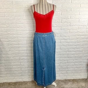 Può includere: Una gonna lunga in denim con uno spacco anteriore e una chiusura con bottone. La gonna è di un lavaggio blu medio e ha una vestibilità rilassata.