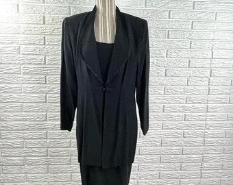 May include: A black dress suit with a long jacket and a skirt. The jacket has a wide collar and a single button closure. The skirt is knee-length.