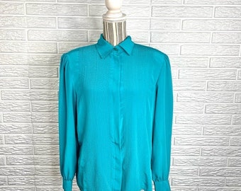 May include: A turquoise blue long-sleeved blouse with a button-up front and a collared neckline. The blouse has a pleated design and is made of a silky fabric.