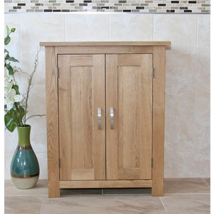 May include: A light wood cabinet with two doors and silver handles. The cabinet is standing on a tiled floor.