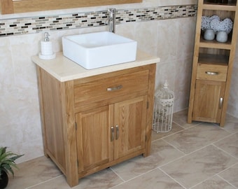 May include: A light wood bathroom vanity with a white ceramic sink and a single drawer and two doors. The vanity is in front of a tiled wall with a decorative mosaic border.