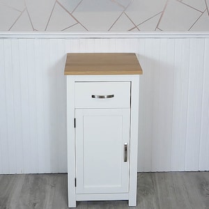 May include: White bathroom cabinet with a single drawer and a door. The cabinet has a wood top and a mirror above it.