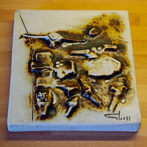 Peut inclure: Un carreau de céramique blanc avec un motif abstrait brun et blanc. Le carreau est texturé et présente un motif en relief. Le carreau est signé "Clauss" dans le coin inférieur droit.