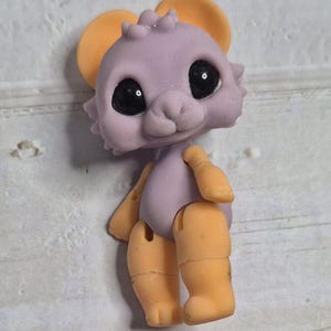 Peut inclure: Une petite souris jouet articul&eacute;e, avec un corps lavande et des oreilles, bras et jambes oranges. Le jouet a de grands yeux noirs et un petit nez rose. Les membres sont articul&eacute;s, permettant le mouvement. Le jouet est con&ccedil;u pour ressembler &agrave; une souris de dessin anim&eacute;.