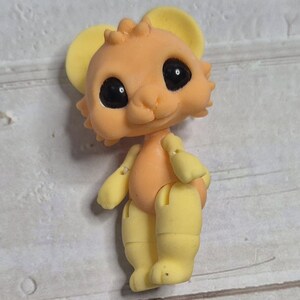 Peut inclure: Petite figurine articul&eacute;e repr&eacute;sentant une souris de dessin anim&eacute;. La souris a un corps couleur p&ecirc;che, des oreilles, des bras et des jambes jaunes, et de grands yeux noirs. La figurine est debout.