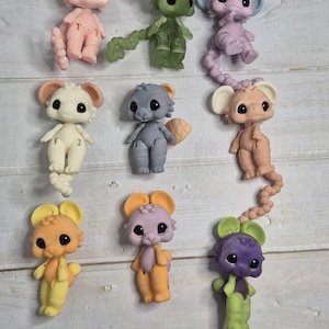 Peut inclure: Neuf figurines de souris color&eacute;es dans diverses nuances de rose, vert, violet, gris, beige et jaune. Chaque souris a de grands yeux noirs et de grandes oreilles. Les figurines sont dispos&eacute;es sur une surface claire imitation bois.