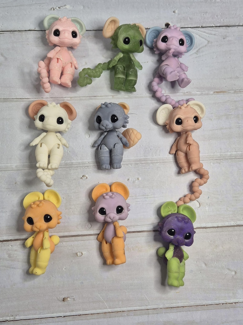 Peut inclure: Neuf figurines de souris color&eacute;es dans diverses nuances de rose, vert, violet, gris, beige et jaune. Chaque souris a de grands yeux noirs et de grandes oreilles. Les figurines sont dispos&eacute;es sur une surface claire imitation bois.