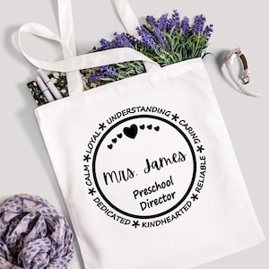 Könnte beinhalten: Weiße Stofftasche mit einem schwarzen Kreisdesign. Der Kreis enthält den Text "Mrs. James Preschool Director" und die Wörter "Ruhig, Loyal, Verständig, Fürsorglich, Engagiert, Gutherzig, Zuverlässig".