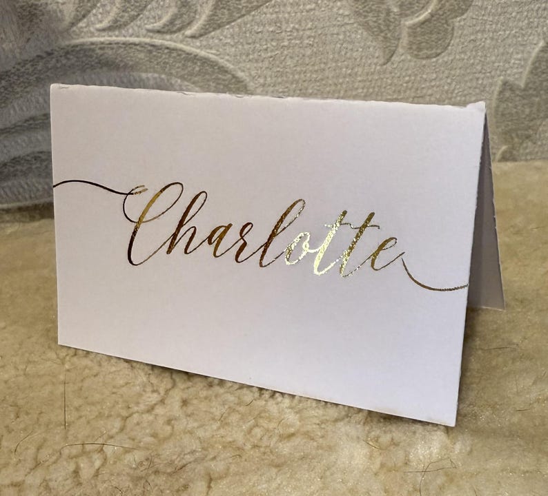 May include: White card with the name "Charlotte" written in gold foil lettering.
