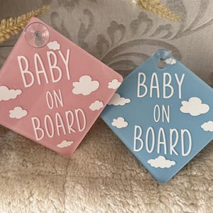 Könnte beinhalten: Zwei Auto-Schilder, eines rosa und eines blau, mit weißen Wolken und dem Text "Baby on Board".