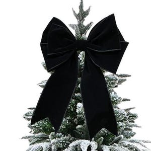 May include: A large, black velvet bow, possibly for Christmas tree decoration, is the focal point. The bow is centered atop a frosted, artificial evergreen tree. The bow's texture and dark colour contrast with the light green and white of the tree.