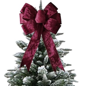 Könnte beinhalten: Eine burgunderrote Samt Schleife mit einer großen, vollen Schleife und langen Bändern, platziert auf einem gefrosteten Weihnachtsbaum.