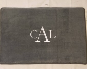 May include: Gray bath mat with the name "CAL" embroidered in white.
