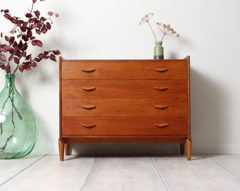 May include: A wooden chest of drawers featuring four horizontal drawers with curved, recessed handles. The piece is constructed from a warm-toned wood with a visible grain pattern and is supported by four tapered legs, showcasing a clean, rectangular frame.