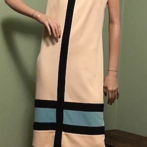 May include: A sleeveless dress with a geometric design in black, white, and blue. The dress has a fitted silhouette and a straight hemline.