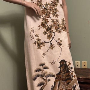 May include: Cream-colored sleeveless dress featuring a Japanese-inspired design. The dress showcases a detailed illustration of a pagoda, trees, and a bridge, with floral accents. The fabric appears to be a linen blend.