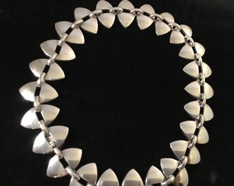 May include: A silver necklace with a chain made of triangular links. The necklace is made of a series of connected triangular shapes.