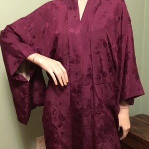 May include: A purple silk robe with a floral pattern. The robe has long sleeves and a V-neck.