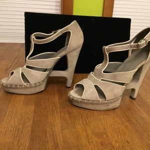 May include: A pair of gray suede platform sandals with a unique open-toe design and a chunky heel.