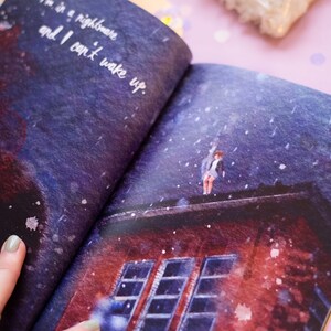 May include: Open book illustration with a surreal scene. A person stands on a rooftop under a dark, snowy sky. Text reads, "I'm in a nightmare and I can't wake up." The book's pages are open, revealing the artwork.