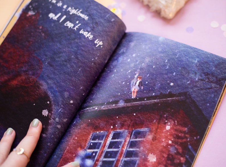 May include: Open book illustration with a surreal scene. A person stands on a rooftop under a dark, snowy sky. Text reads, "I'm in a nightmare and I can't wake up." The book's pages are open, revealing the artwork.