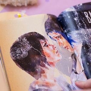May include: Open book with watercolor illustrations of two figures with dark hair and blue hair. The figures are facing each other with a soft, emotional expression. The page has the text "BAY OR" in white.