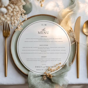 Puede incluir: Una mesa formal con una tarjeta de menú. La tarjeta de menú es blanca con texto negro y un diseño circular. Se ven cubiertos dorados y un plato verde claro. El menú enumera aperitivos, platos principales y postres.