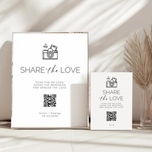May include: Two white signs with the text "SHARE the LOVE" and a camera icon. The larger sign includes the names "Susan + George" and a date. Both signs have a QR code and the text "SCAN THE QR CODE. SHARE THE MEMORIES. AND SPREAD THE LOVE."