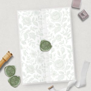 Puede incluir: Un conjunto de invitaciones de boda con un diseño floral en verde claro. La invitación está sellada con un sello de cera verde. También se ven un joyero y una cinta blanca.