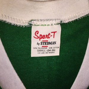Pu&ograve; includere: Maglietta verde e bianca con un'etichetta bianca che recita "Sport-T by Stedman 50% Polyester - 50% Cotton Small (34-36) For Care See Reverse"