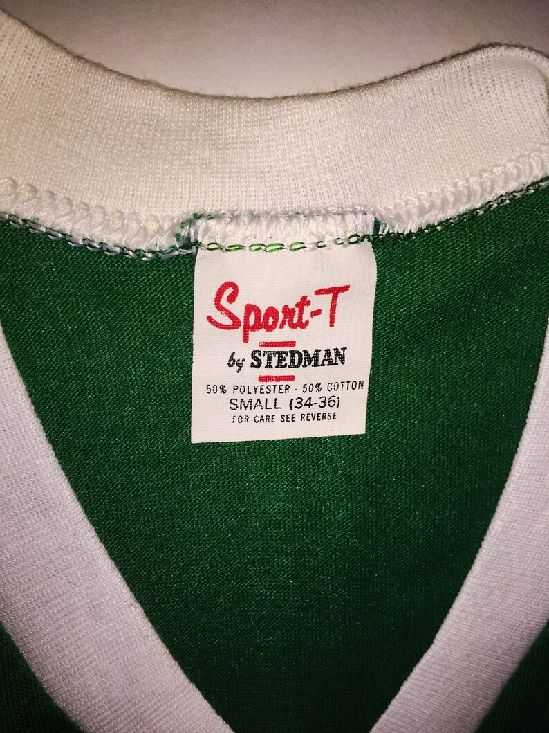 Pu&ograve; includere: Maglietta verde e bianca con un'etichetta bianca che recita "Sport-T by Stedman 50% Polyester - 50% Cotton Small (34-36) For Care See Reverse"