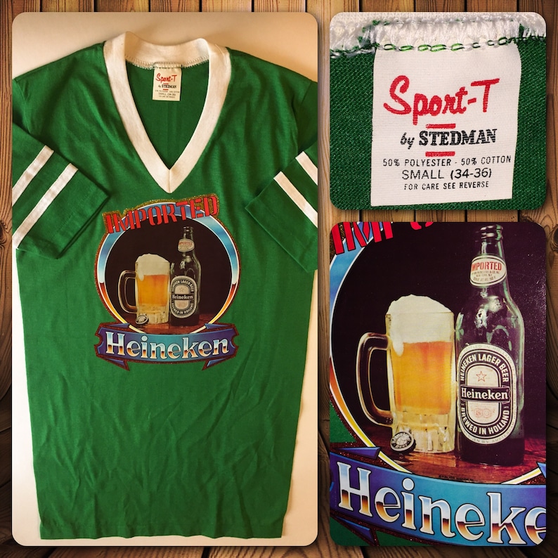 Pu&ograve; includere: Maglietta verde a maniche corte con strisce bianche sulle maniche e un collo a V bianco. La maglietta presenta una grafica di una boccale di birra e una bottiglia con il testo "IMPORTED" e "Heineken". L'etichetta sulla maglietta recita "Sport-T by Stedman 50% Polyester - 50% Cotton Small (34-36) For Care See Reverse".