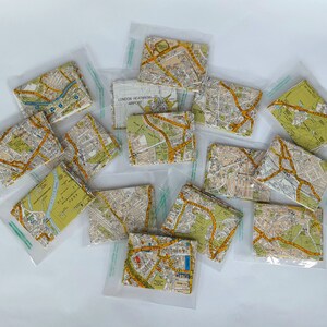 May include: A collection of small, clear plastic bags containing folded maps of London, England. The maps are printed in yellow and brown with street names and landmarks. The bags are arranged on a white surface.