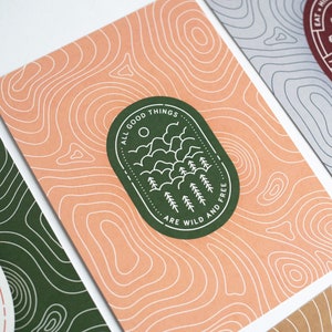 Könnte beinhalten: Ein Satz von vier Karten mit einem topografischen Kartendesign. Jede Karte hat eine andere Farbe und ein einzigartiges Zitat. Das Zitat auf der gezeigten Karte lautet "All good things are wild and free".
