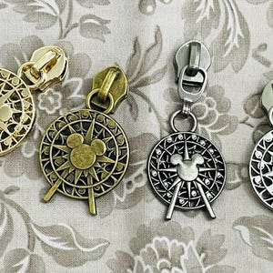 May include: Four metal zipper pulls with compass and Mickey Mouse designs. The pulls are in gold, antique brass, and silver tones. The compass design features a Mickey Mouse head in the center and directional lines.