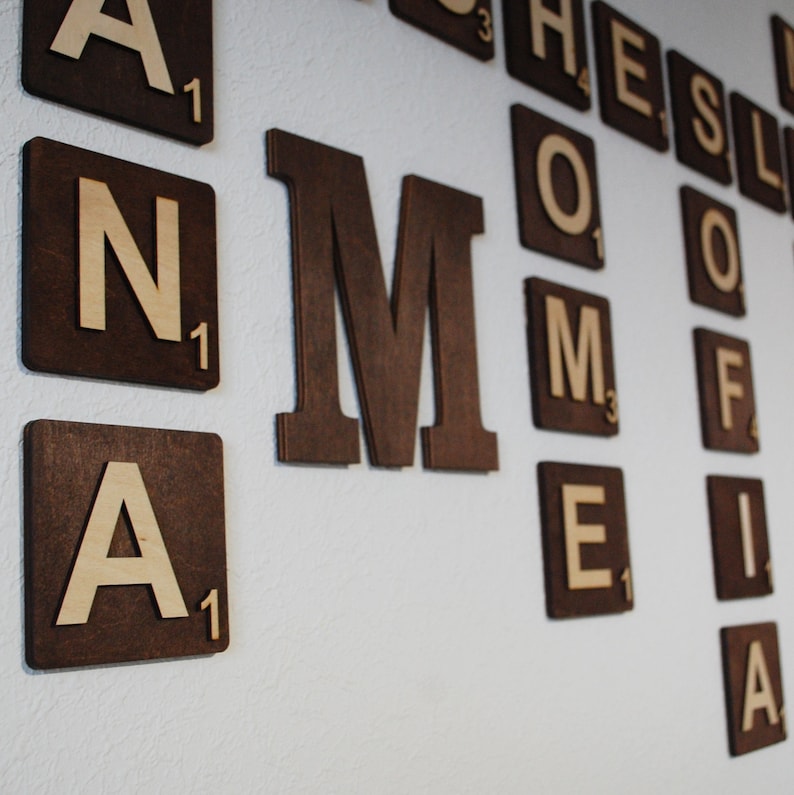 Puede incluir: Una pared decorada con fichas de Scrabble de madera que deletrean la palabra "MOM" en letras grandes. Las fichas son marrones con letras y n&uacute;meros blancos.