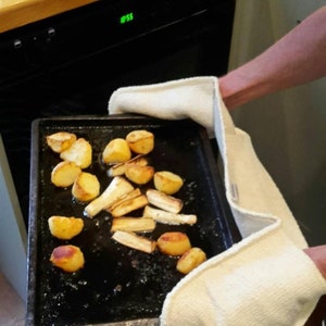 May include: A black baking sheet holds roasted potatoes and parsnips. The vegetables are golden brown and appear freshly cooked. The sheet is held with white oven mitts, suggesting a hot dish just out of the oven.