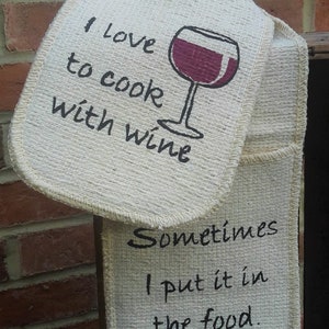 May include: Two white cotton pot holders with black text. The top pot holder has a red wine glass graphic and the text "I love to cook with wine". The bottom pot holder has the text "Sometimes I put it in the food."