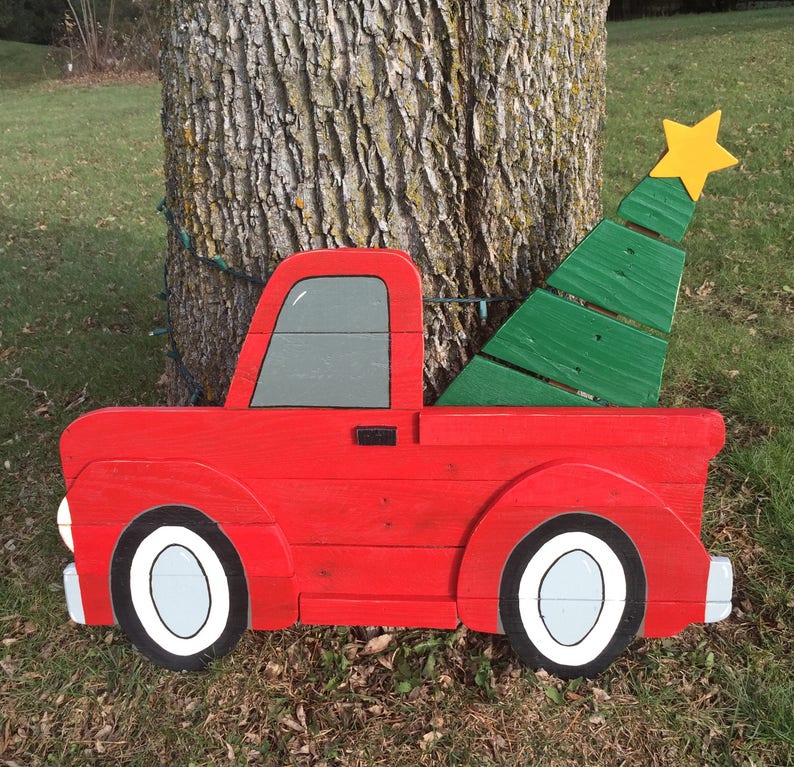 May include: A red wooden pickup truck with a green wooden Christmas tree in the bed. The truck has white wheels and a gray window. The tree has a yellow star on top.