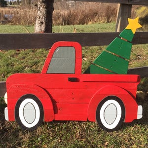 May include: A red wooden pickup truck with a green wooden Christmas tree in the bed. The truck has white tires and a gray window. The tree has a yellow star on top.