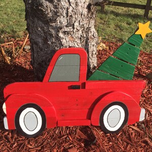 May include: A red wooden pickup truck with a green wooden Christmas tree in the bed. The truck has white tires and a gray window. The tree has a yellow star on top.