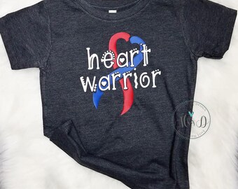 May include: A dark grey t-shirt with a red and blue ribbon design and the text "heart warrior" in white.