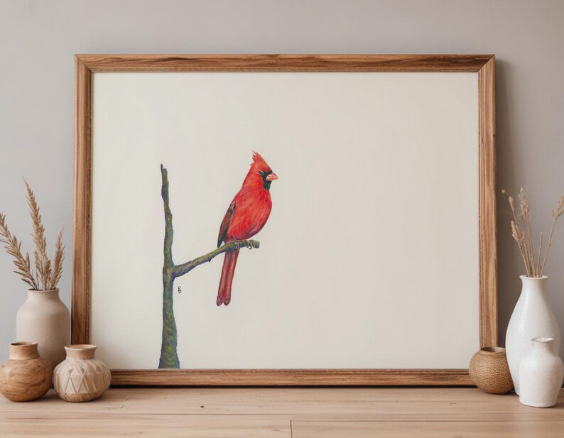 May include: A framed print featuring a vibrant red cardinal perched on a branch. The bird is set against a cream-colored background, framed by a natural wood frame. The artwork evokes a sense of nature and tranquility, suitable for home decor.