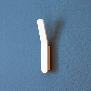 Könnte beinhalten: Ein weißer Plastikhaken, der an einer blauen Wand befestigt ist. Der Haken ist gebogen und hat eine flache Basis.