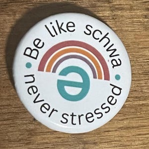 May include: White button with a rainbow design and the text "Be like schwa, never stressed".